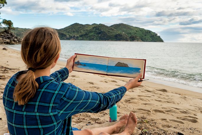 一位妇女坐在沙滩上，手里拿着一幅画