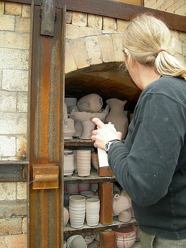 Person loading a large wood-fired kiln with pottery