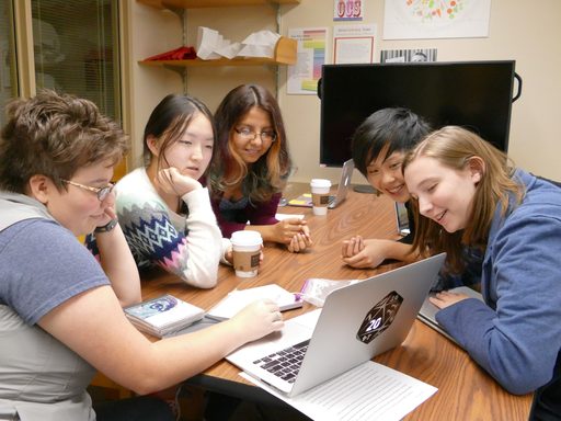 Five students sit at a table looking at a laptop