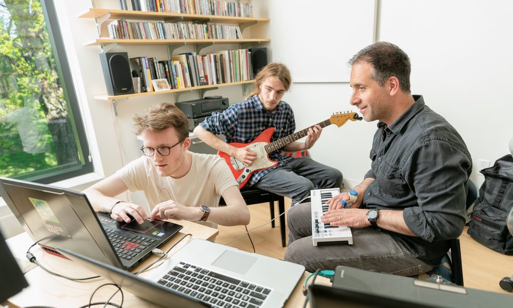 Two students and a professor compose music in an office