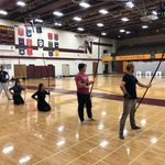 Kyudo Practice. Several students are lined up in a school gym with longbows
