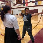 Kyudo Practice. A student draws an arrow as instructor Carly Born looks on