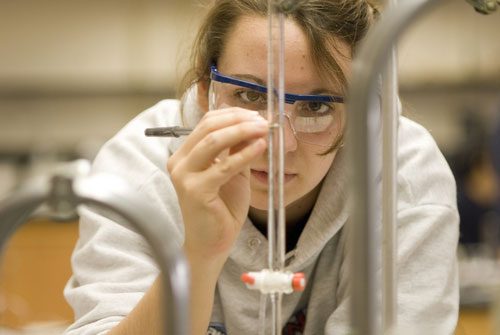 a woman wearing safety glasses conducts an experiment in a laboratory