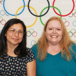 Two staff members in front of the Olympic flag