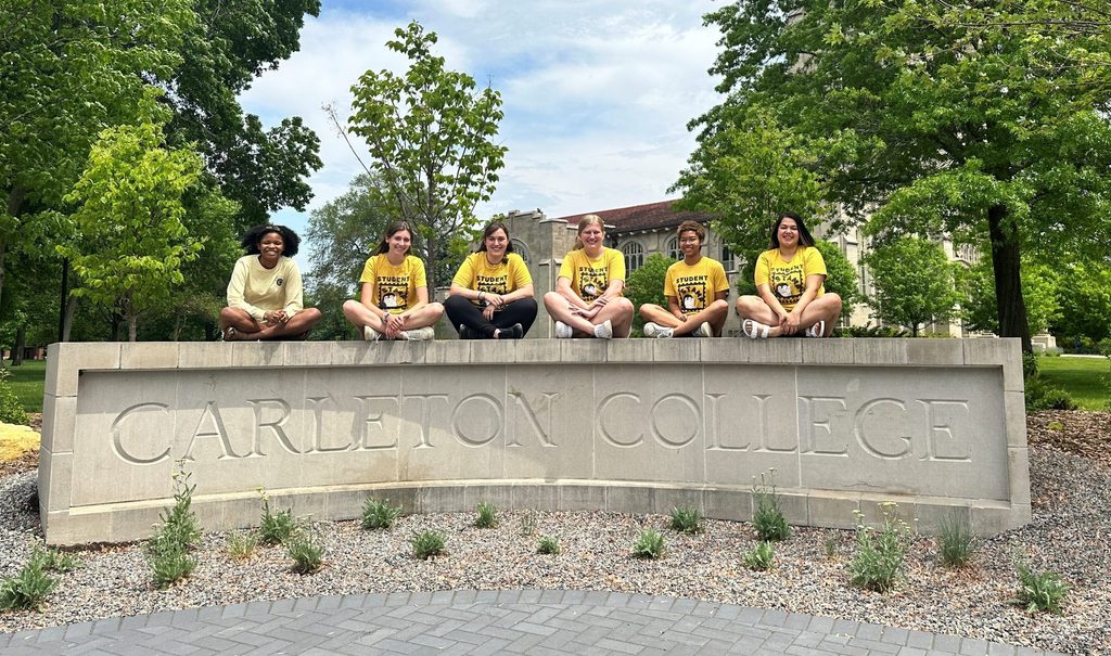 students sitting on the Carleton College sign