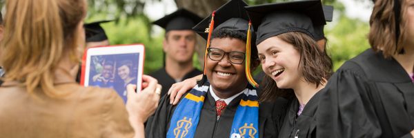 Two students pose for a photograph during commencement. They are wearing traditional graduation caps and gowns.