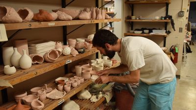 A student places a ceramic bowl on a shelf