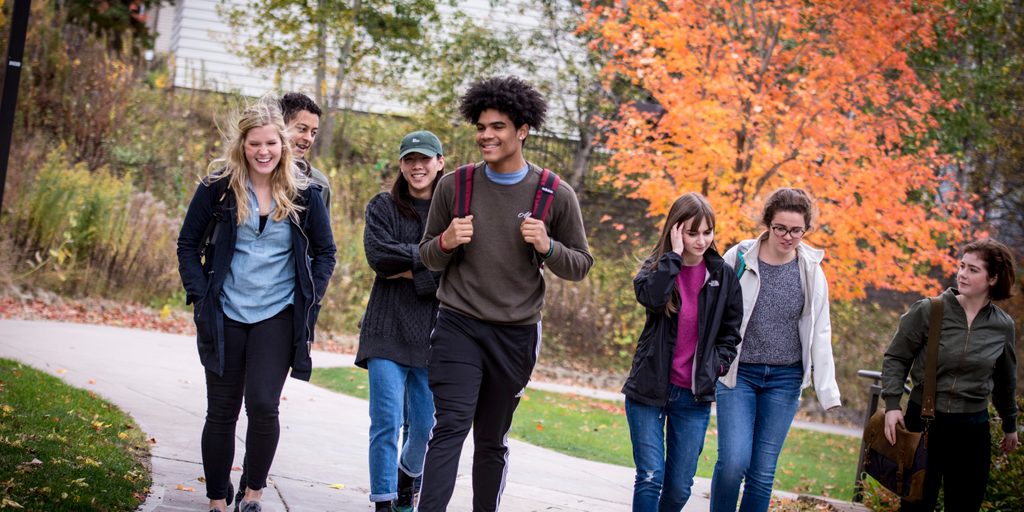 A group of students walks towards the camera, smiling and carrying backpacks
