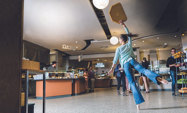 A student holding a tray dances en pointe in East Dining Hall
