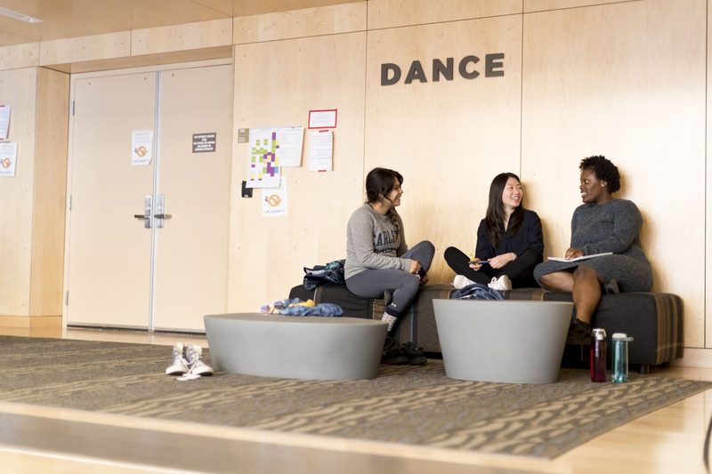 Three students have a conversation outside a dance studio.