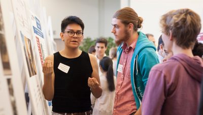 <p>Students have a conversation during a poster session for student research and externship positions</p>