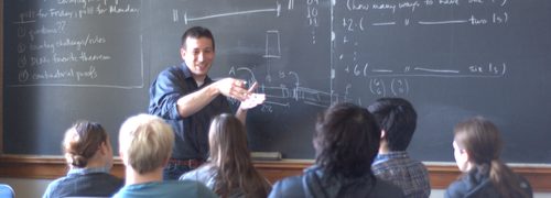 A professor in front of a blackboard, speaking to a group of seated students