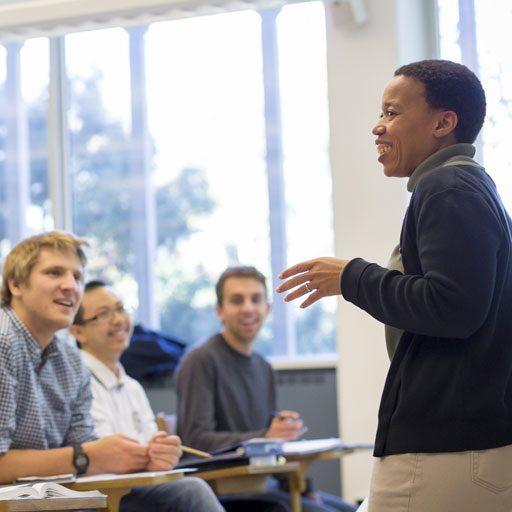 Students smile in class while a professor leads a lesson