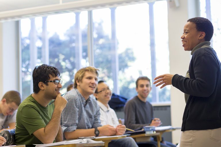 Students smile in class while a professor leads a lesson
