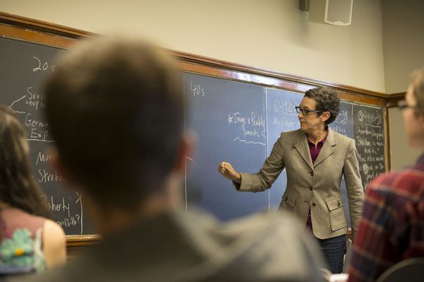 A professor writes on a blackboard in front of a class of students