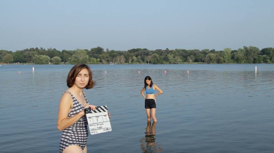 two women in a lake, closer woman holding a film slate and looking at the camera