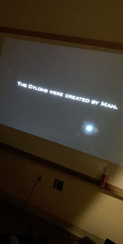 Photo of opening scene of Battlestar Galactica projected onto a whiteboard, with a title card reading "The Cylons were created by Man."