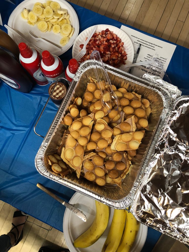 A table with a pan of waffles, bananas, whipped cream, and other toppings