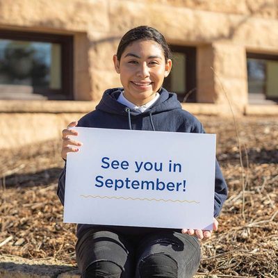 A student smiling and holding a sign that reads "See you in September!"