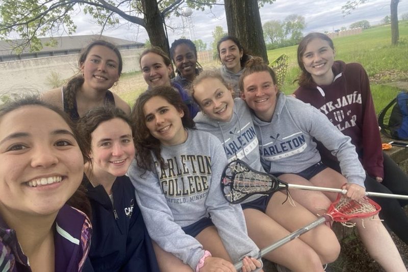 A selfie of the women's lacrosse team outside by the lacrosse field