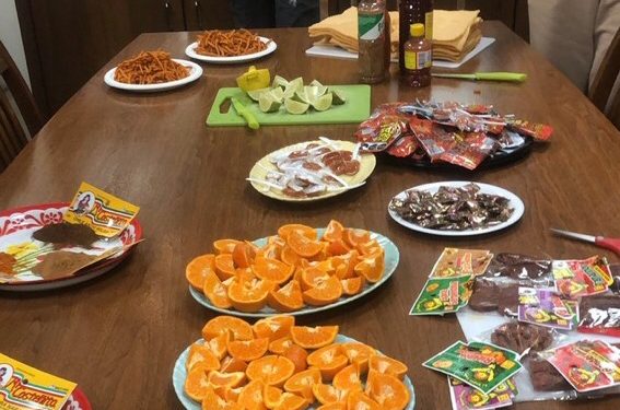 oranges, limes, chilies, crackers, and other snacks spread on a wooden table