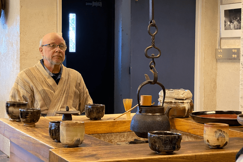 Man sitting at a table with numerous tea bowls leading a tea ceremony