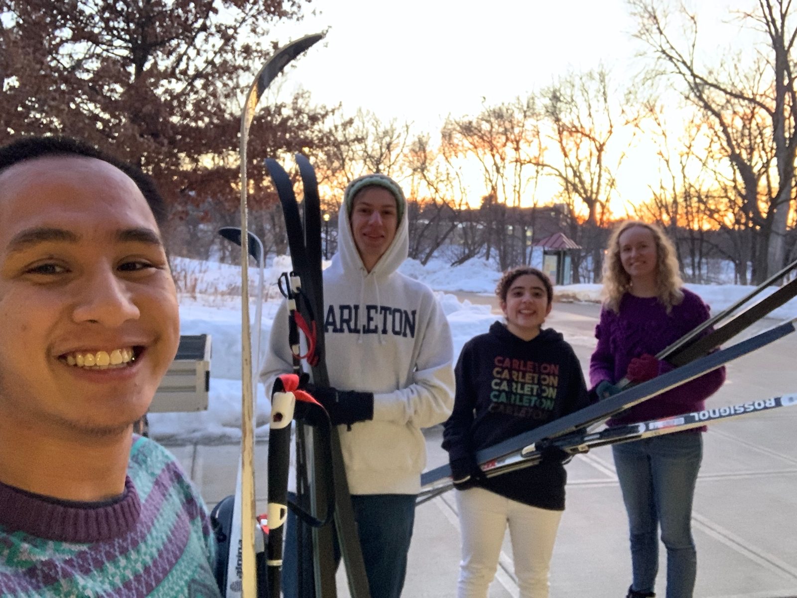 Selfie. Students hold their cross-country skiing equipement while the sun sets on the background.