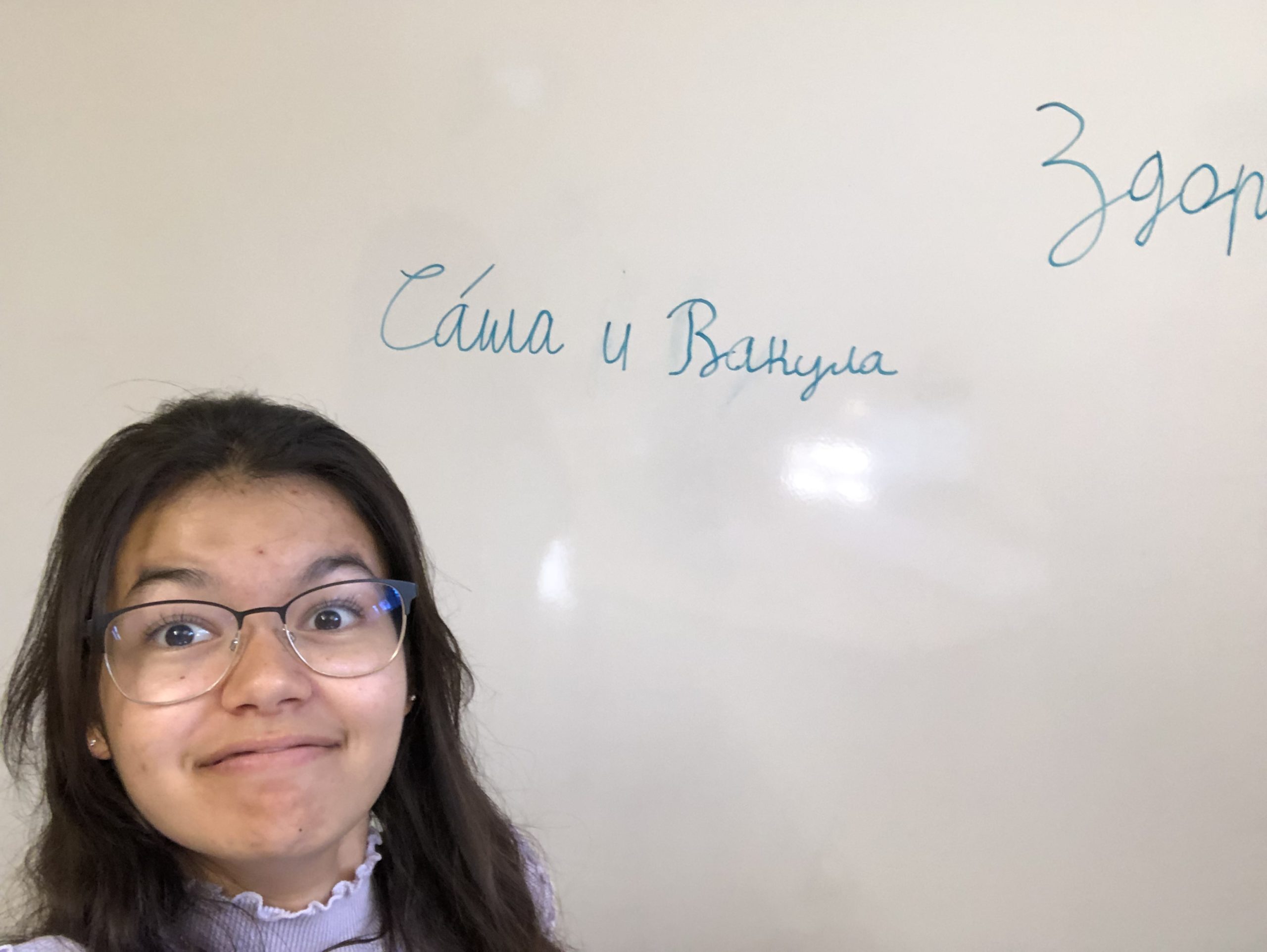 Student poses in front of their Russian name written in cursive