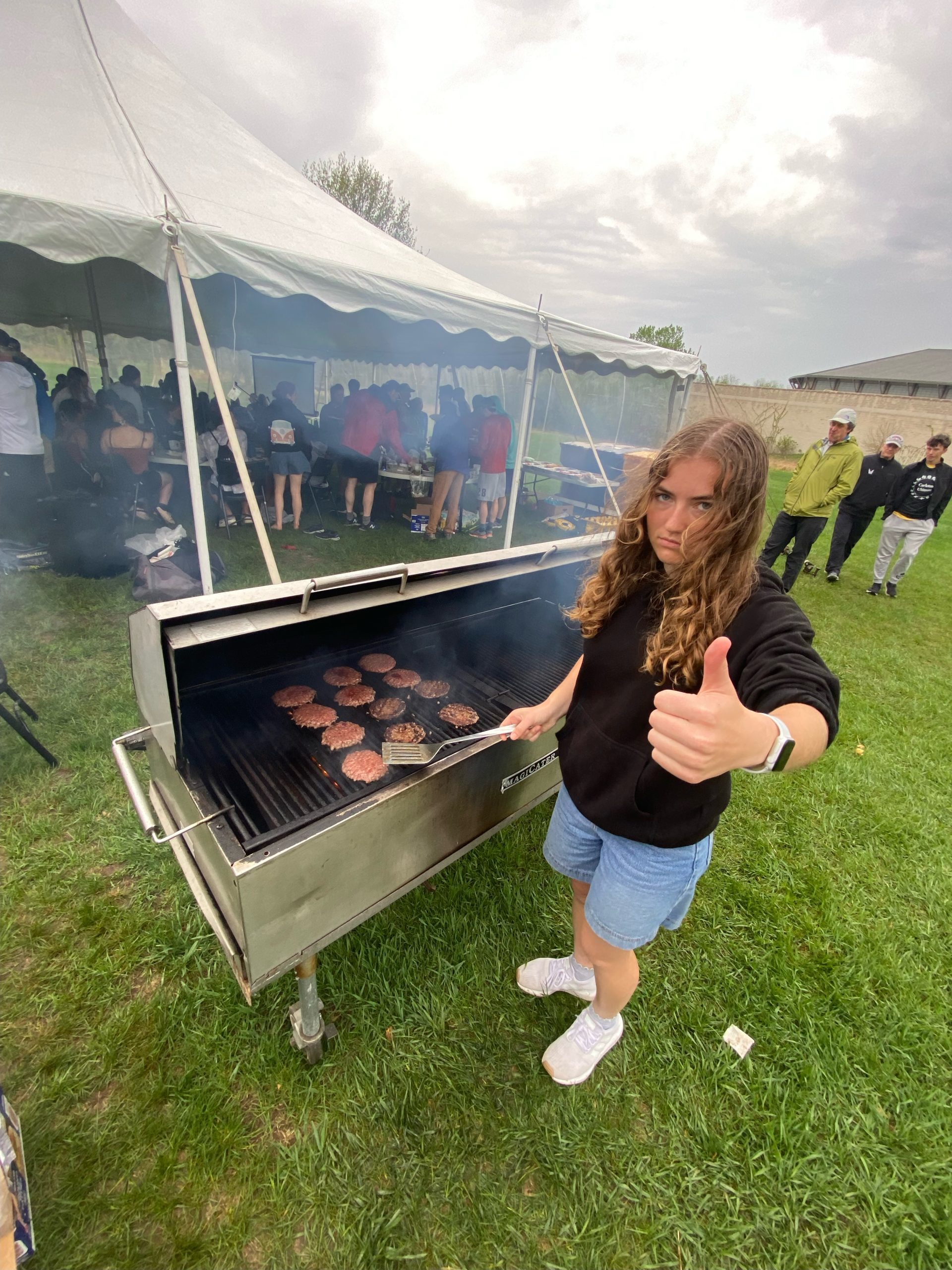 Person standing by a grill holding spatula and giving a thumbs up