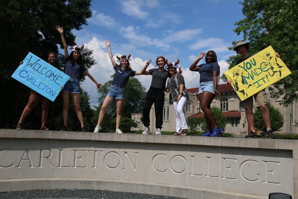 Students holding welcome signs on top of the Carleton College sign
