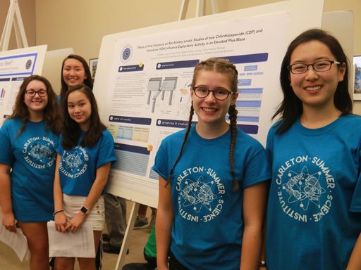 Five science students posing by their poster at the science poster session. All are wearing their blue science institute t-shirts
