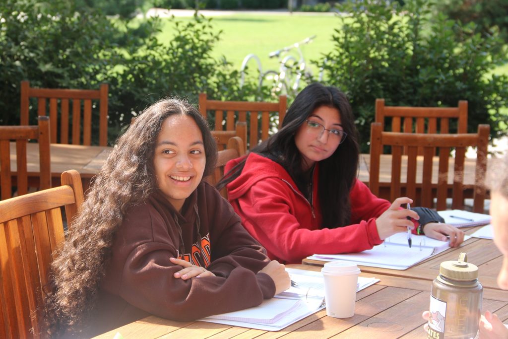 A global pandemics student sits outside at a picnic table with their class materials smiling.