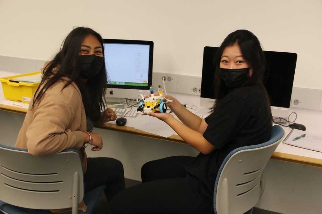 Two Computer Science students smile and hold up their robot