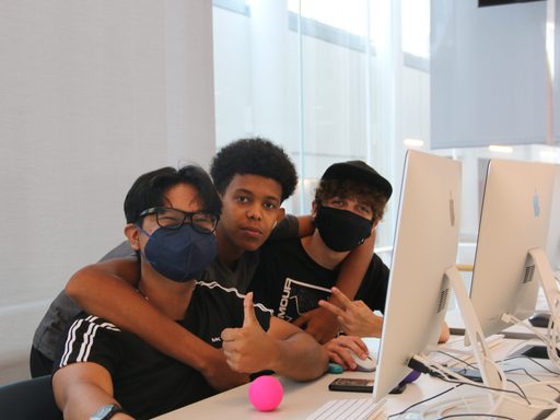 Three students sitting at a computer with their arms around each other's shoulders smiling at the camera.