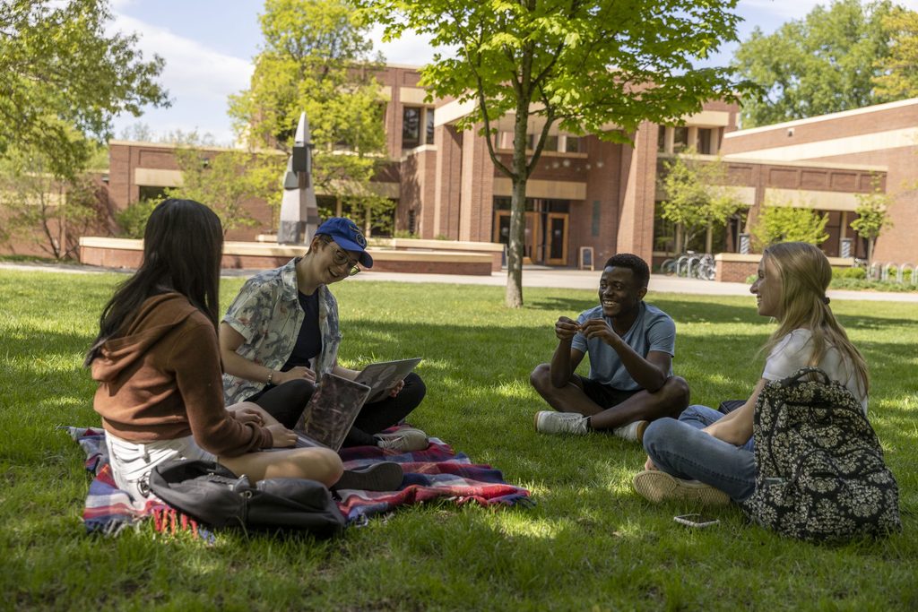 Four Carleton students sit on the grass outside the Library