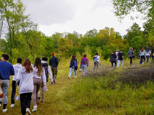 A line of students hikes up a grassy trail through the woods