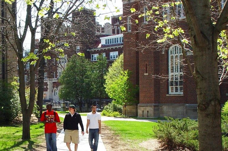 3 students walk on a sidewalk between buildings