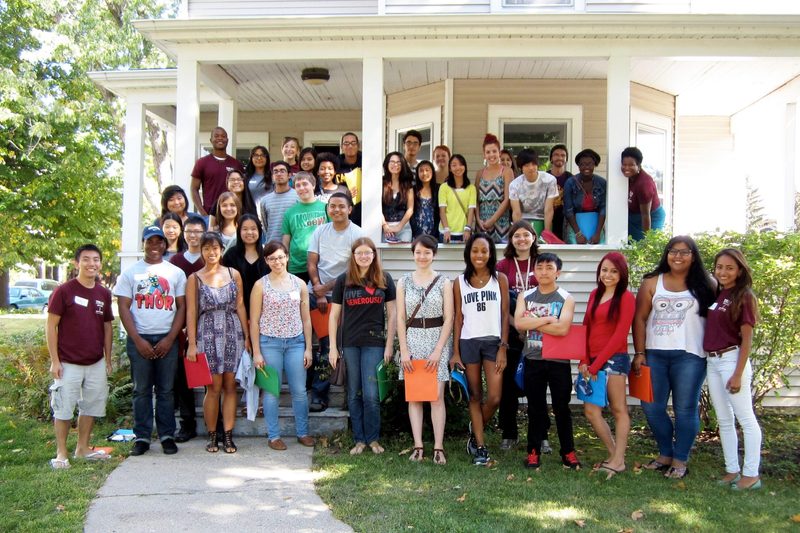 A large gathering of students pose in front of an old house
