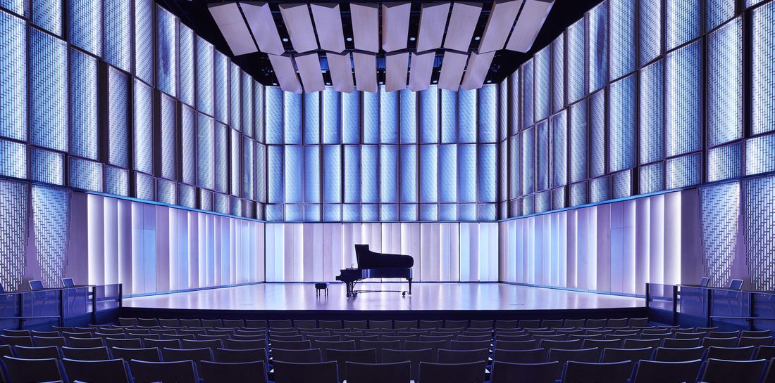 View of the Kracum Performance Hall stage with blue back lighting and a piano at center stage