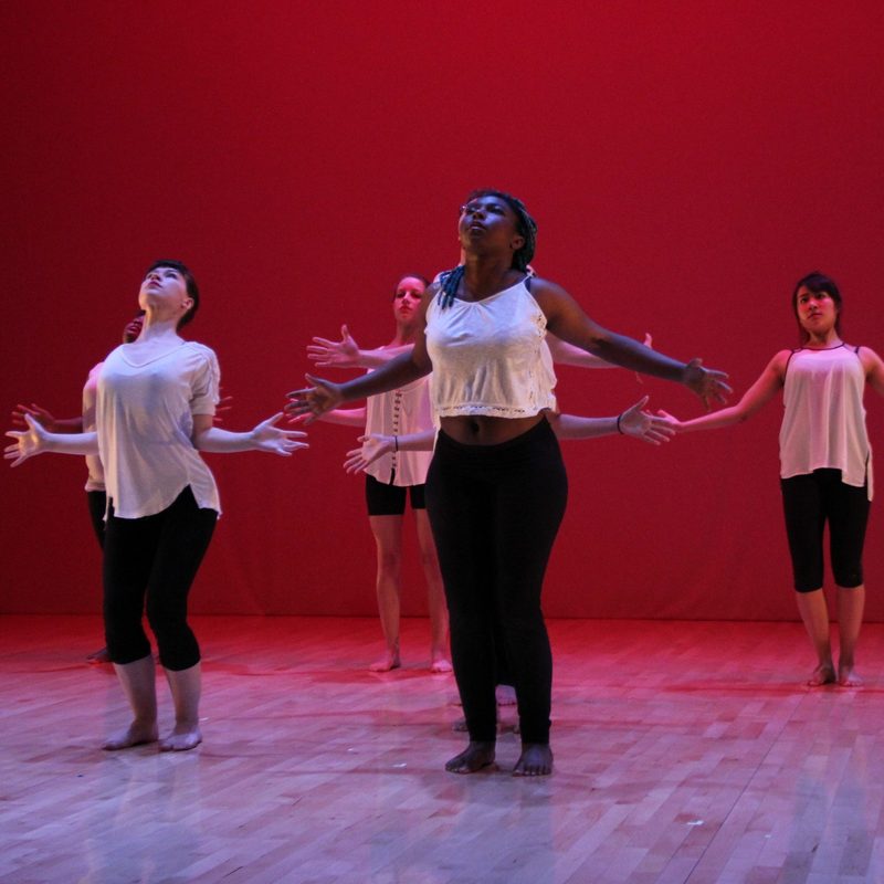 Group of dancing performers on the stage with red lighting and backdrop