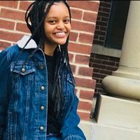 Black female college student sitting on the steps outside a brick building.