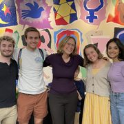 Five people with their arms around each other pose in front of a colorful mural