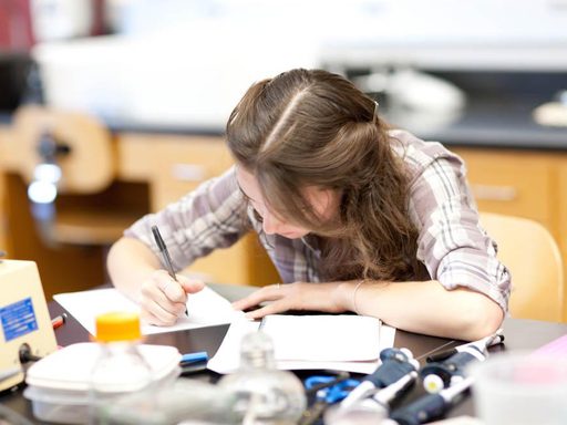A student writes on a sheet of paper in a biology lab