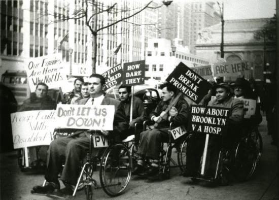 group of protesters in wheelchairs on a sidewalk