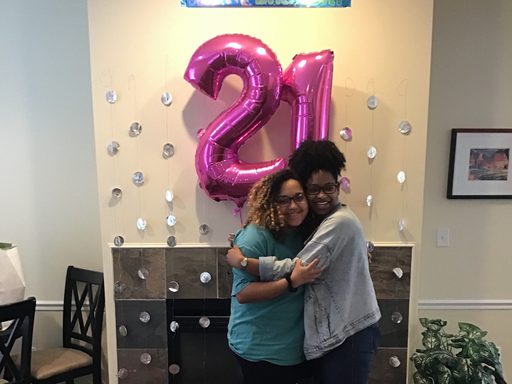 two women hug beneath a happy 21st birthday banner