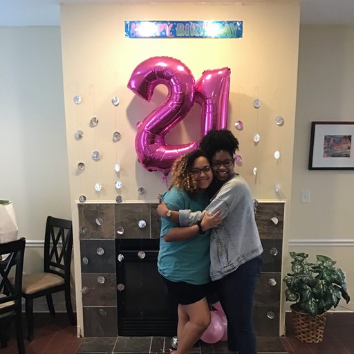 two women hug beneath a happy 21st birthday banner