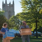 A student and adult with moving boxes with the chapel in the background.