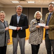 Four smiling people hold checks