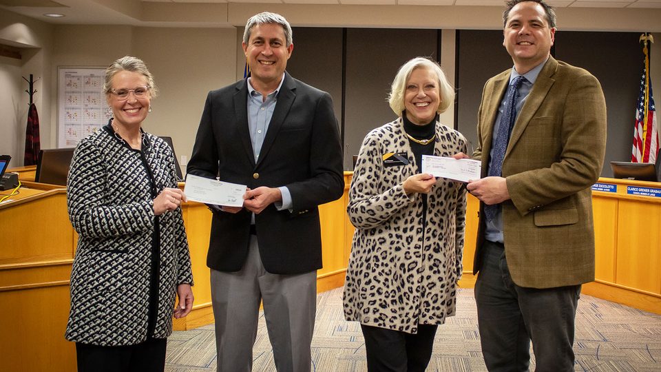 Four smiling people hold checks
