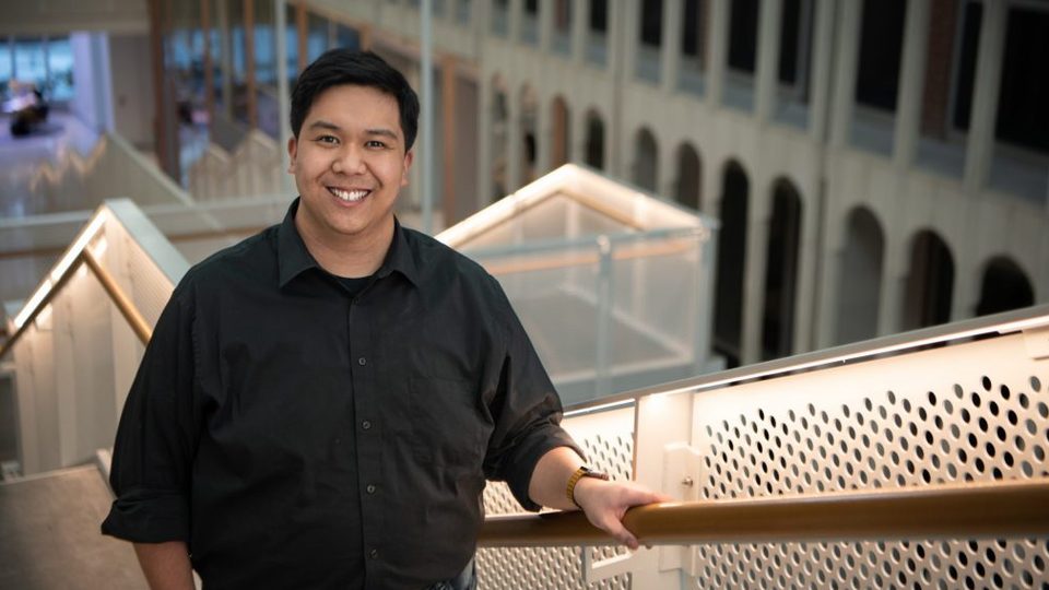 Male college student smiles inside an academic building.